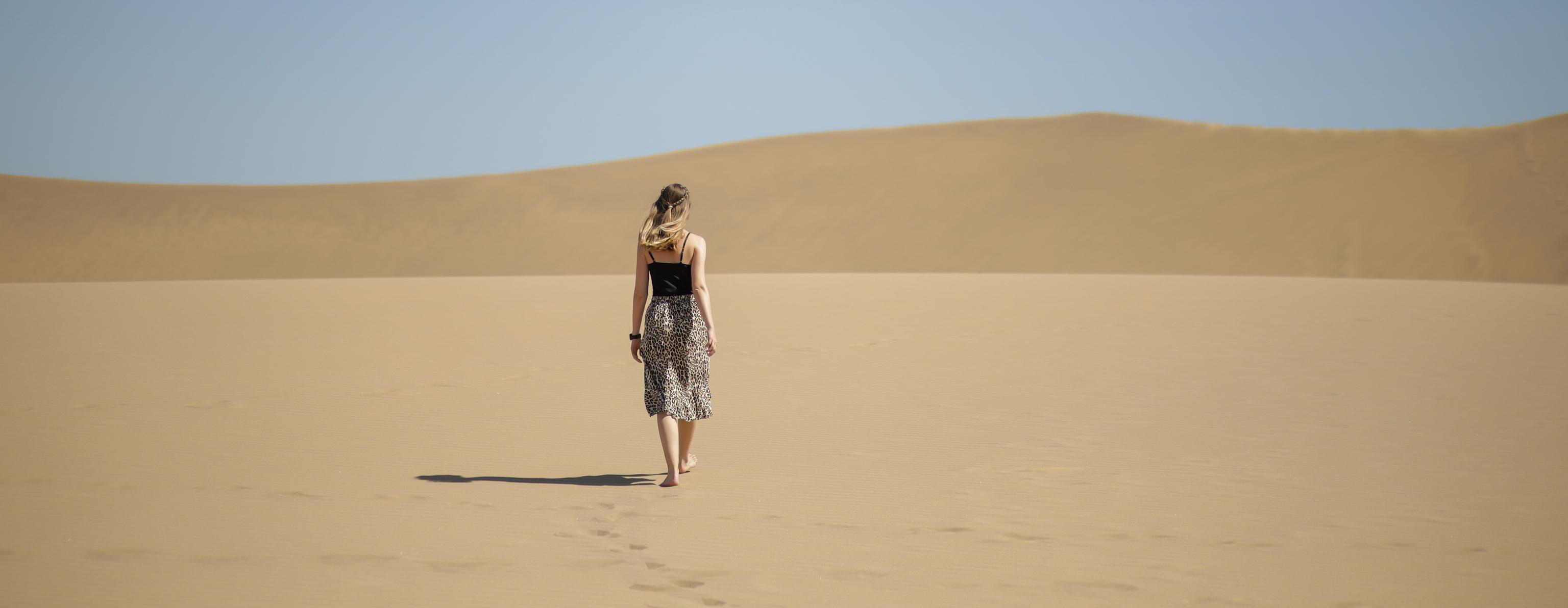 Sophie geht durch eine Wüste mit Dünen im Hintergrund.