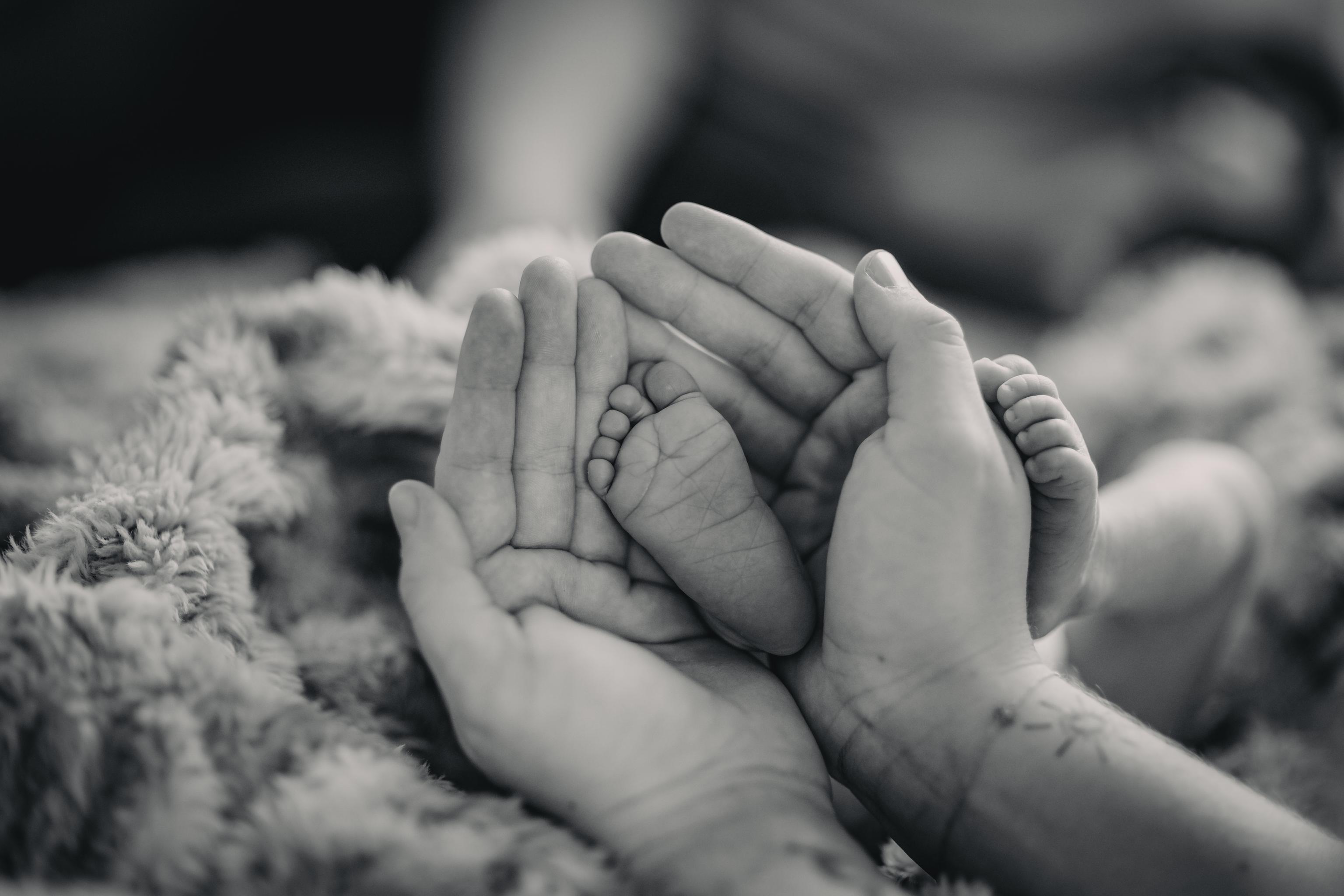 Schwarz-weiß Bild von zwei Händen die einen Babyfuß halten.